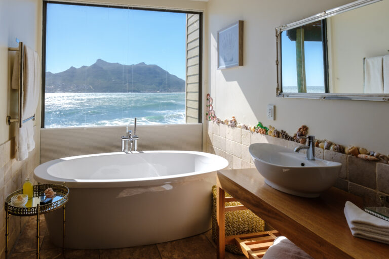 Freestanding bath beside open windows overlooking the ocean in Cape Town.